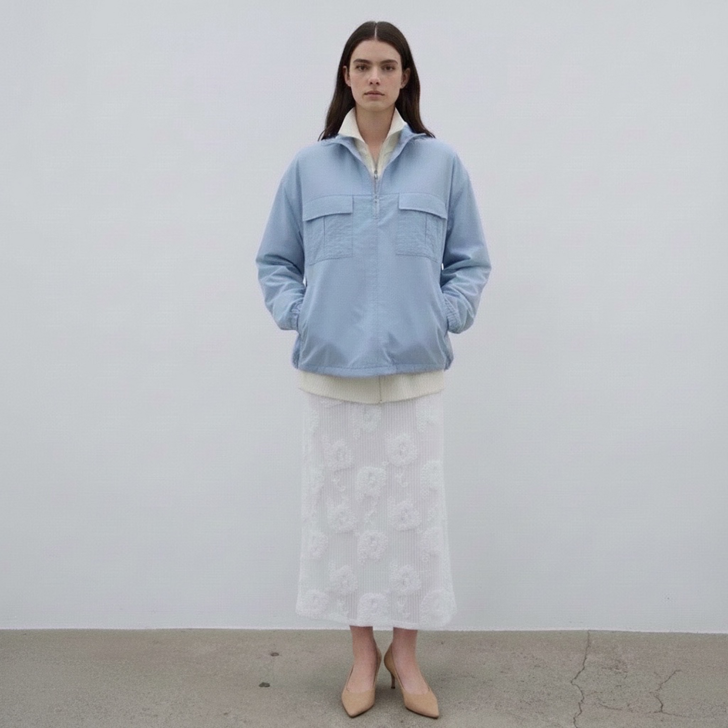 Person wearing a light blue jacket and white dress against a plain background