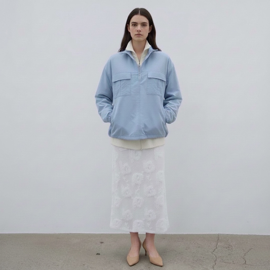 Person wearing a light blue jacket and white dress against a plain background