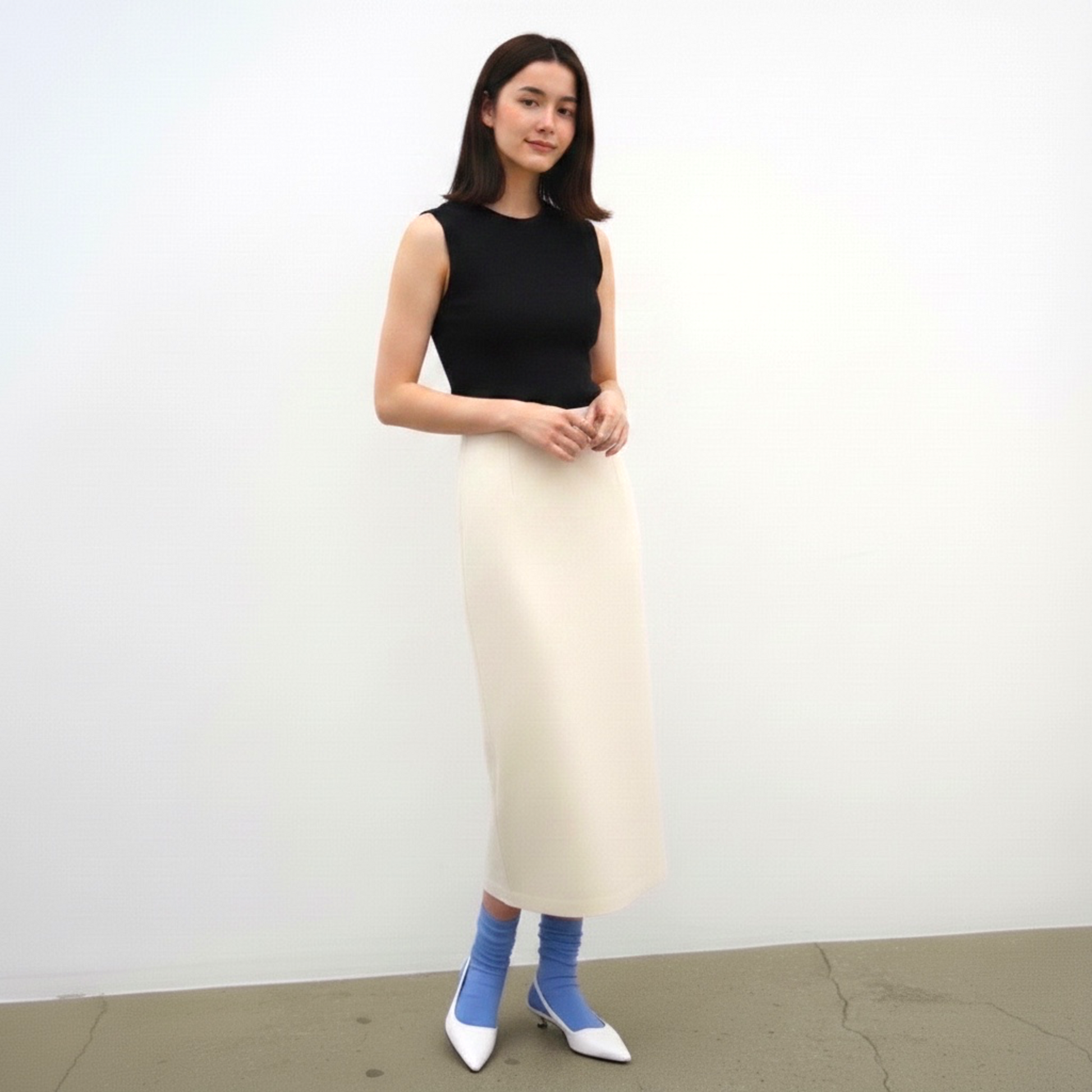 Woman wearing a black sleeveless top and cream skirt against a white background