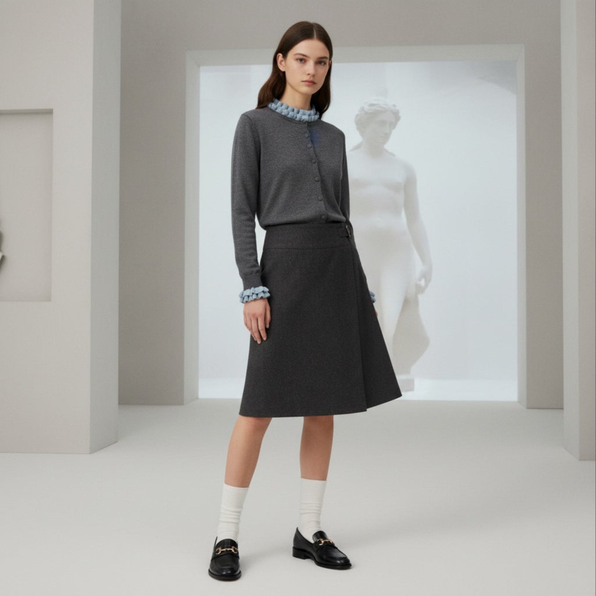 Woman in a gray outfit standing in a minimalistic room with a statue in the background