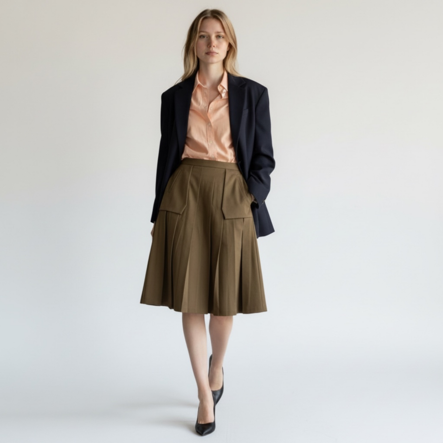 Woman wearing a black blazer, pink blouse, and brown skirt on a white background