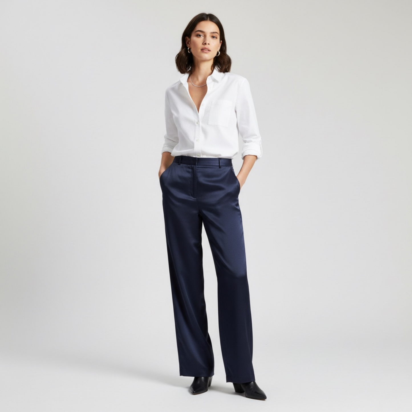 Woman wearing a white shirt and navy pants on a light gray background