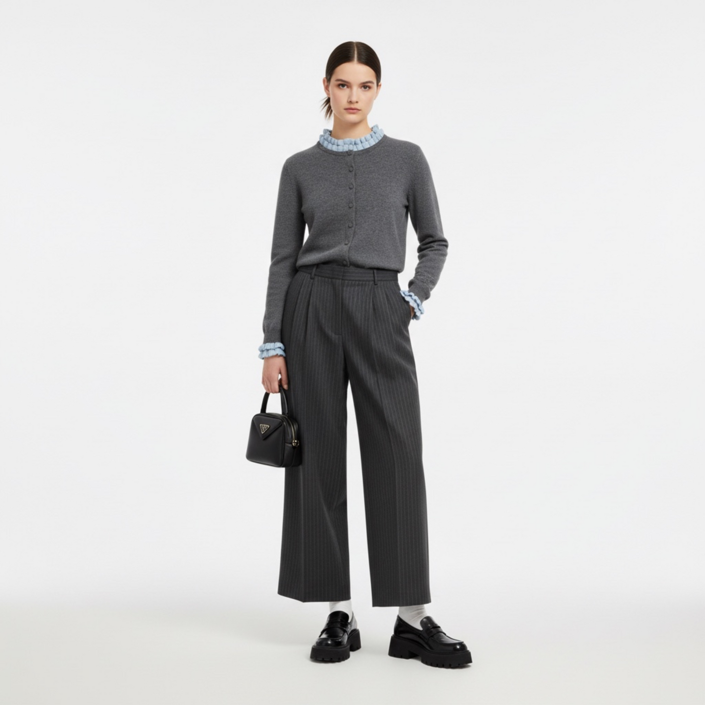Woman wearing a grey sweater and pants with a black handbag on a white background