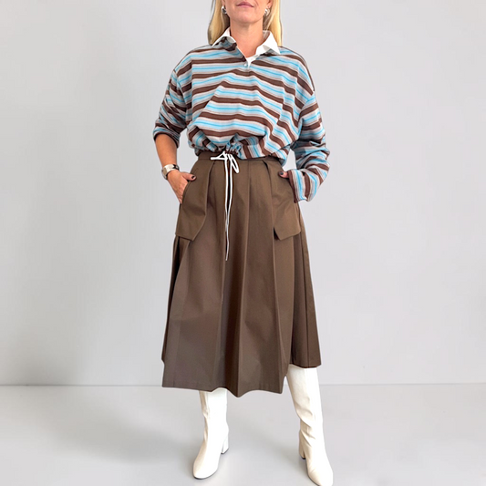 An image of a woman wearing striped blue and brown top, brown midi skirt and white boots