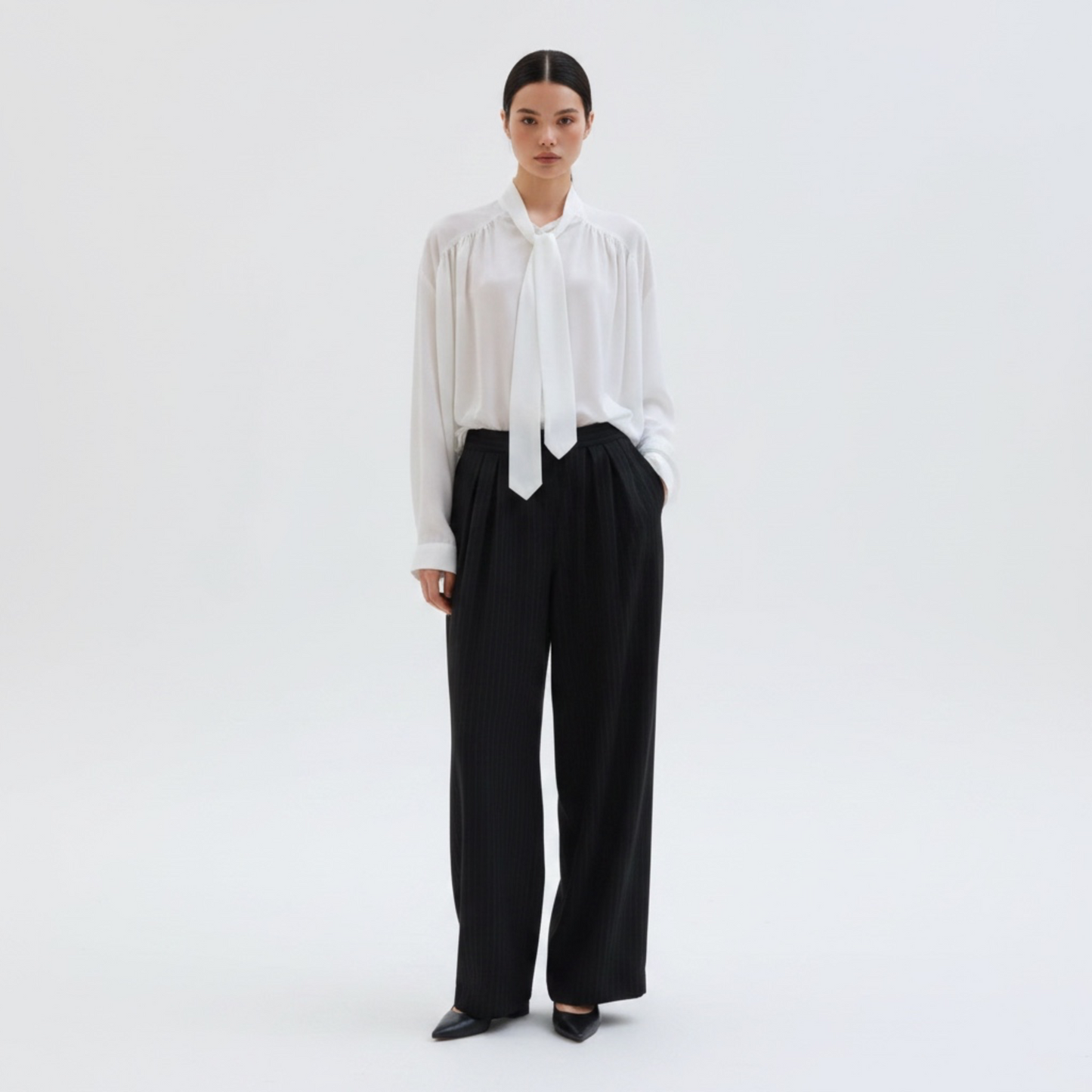 Person wearing a white blouse with a tie and black pants on a white background