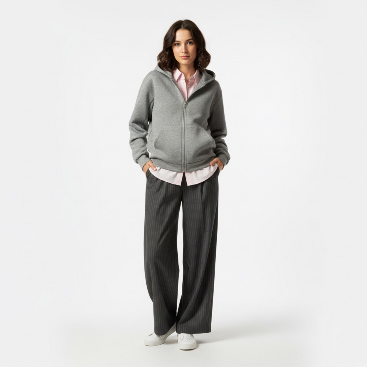 Woman wearing a gray hoodie and dark pants on a white background