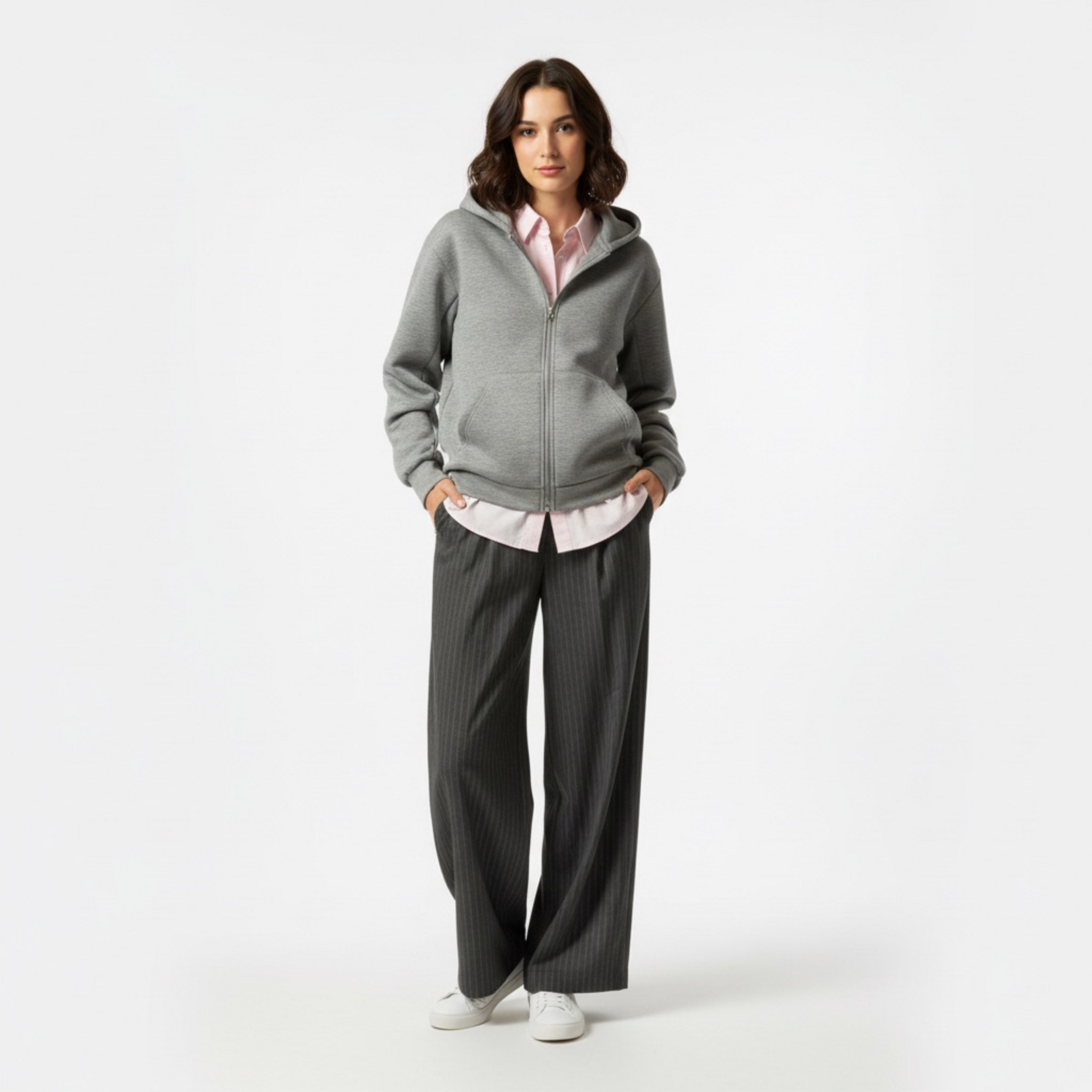 Woman wearing a gray hoodie and dark pants on a white background